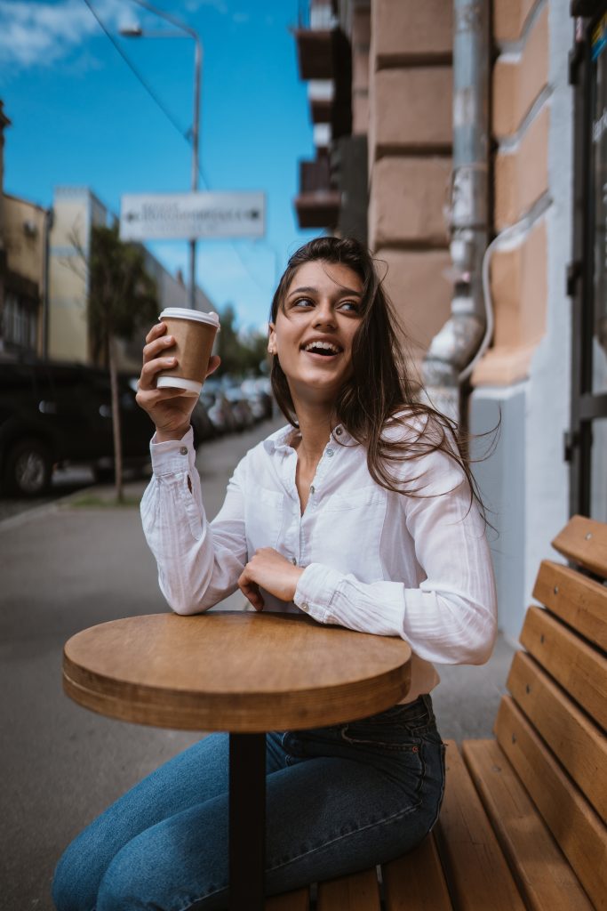 Beautiful young woman in street cafe drinks coffee, outdoor